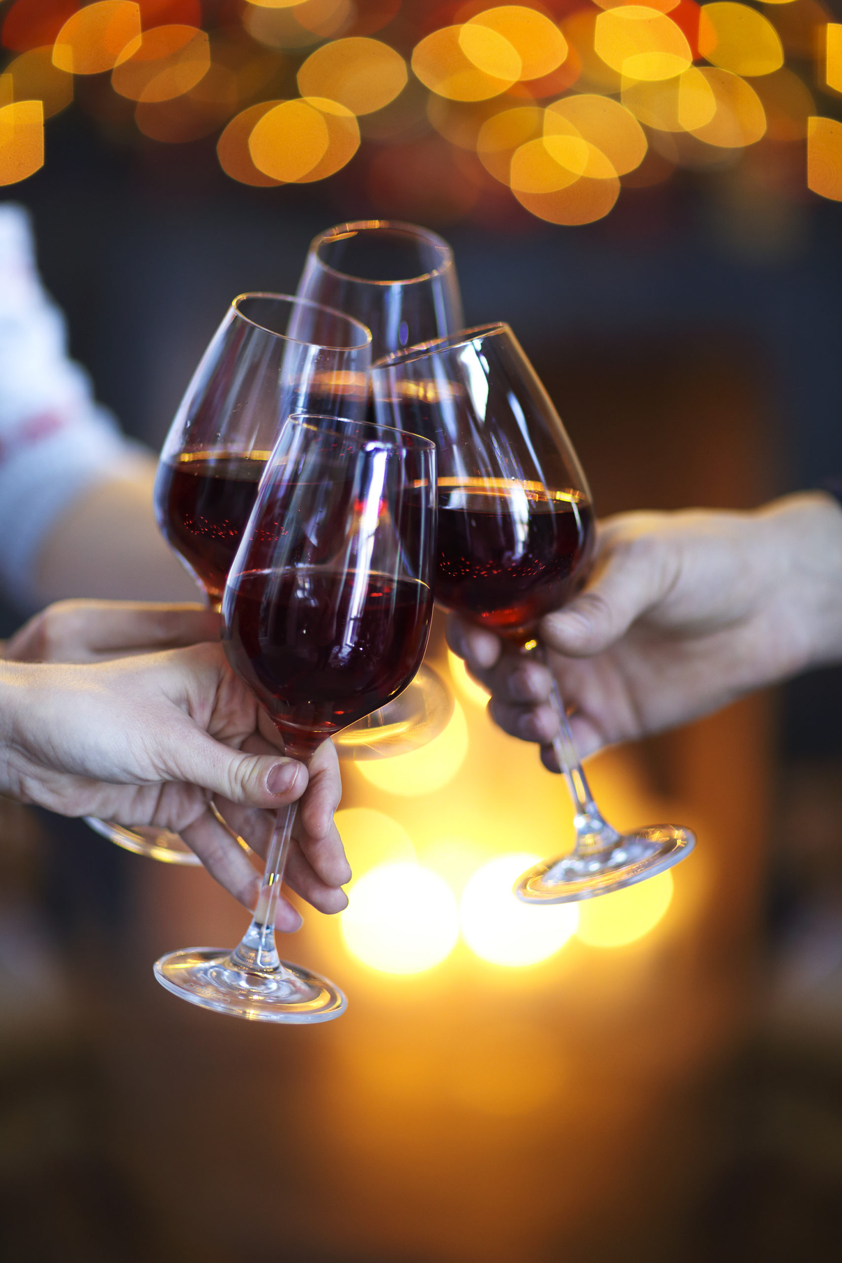 Clinking glasses of wine in hands on bright lights background